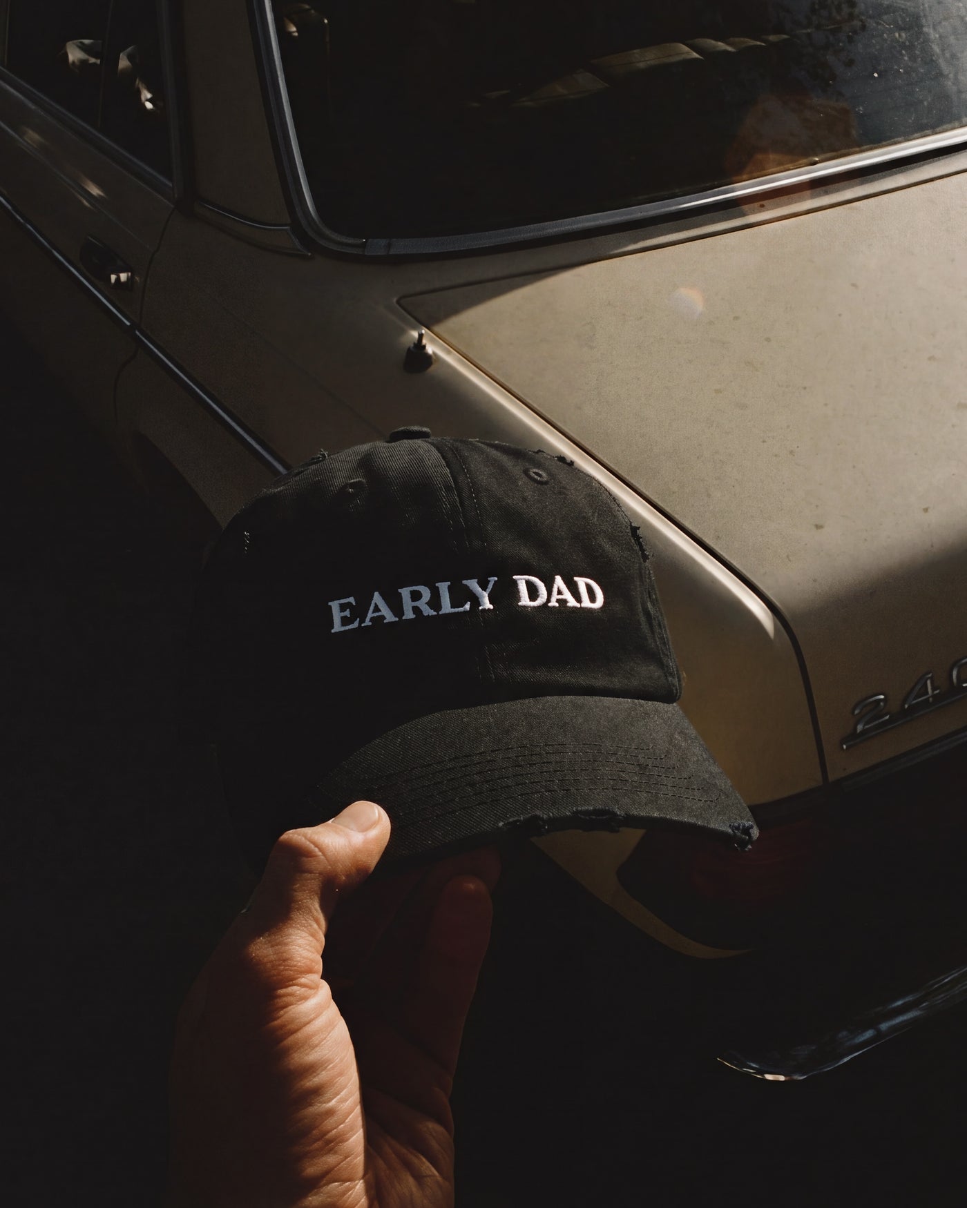 Black Early Dad cap held in front of a vintage car